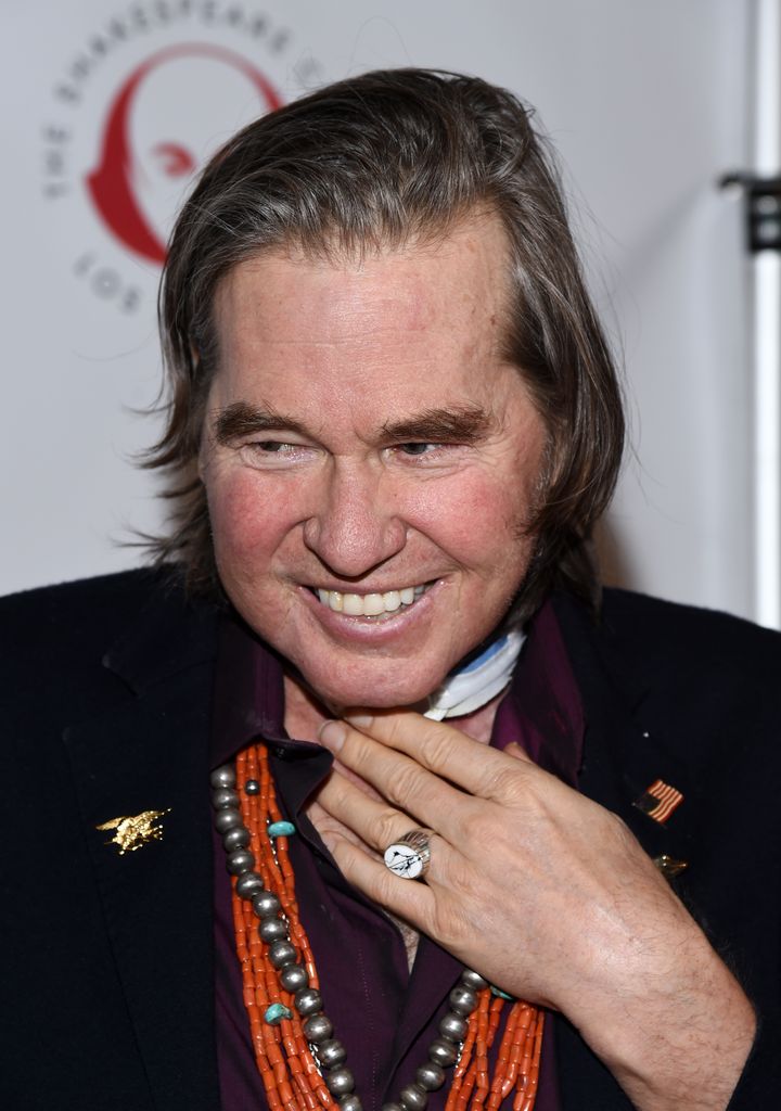 Val Kilmer smiling and holding hand on throat