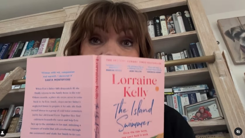 Lorraine Kelly holds up copy of her book while filming in her home office