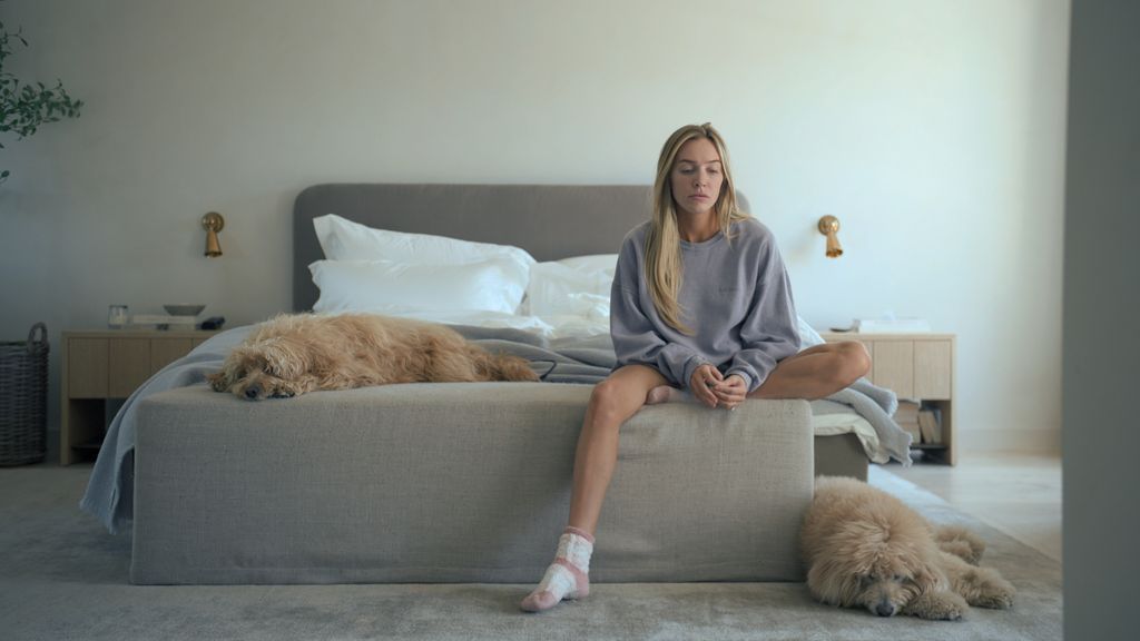 blonde woman sitting on edge of bed in bedroom