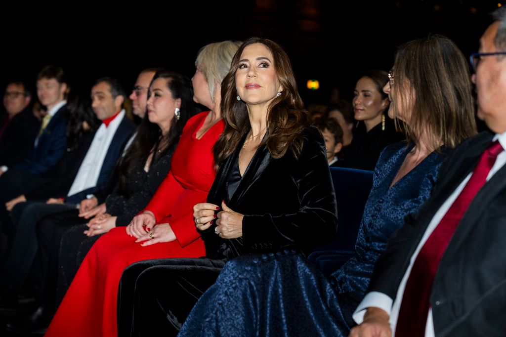 Queen Mary sitting in dark room in crowd
