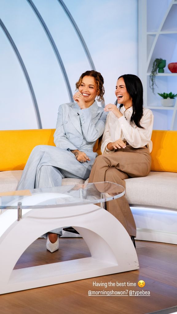 Rita and Anna take over another morning show set, the singer glowing in pastel blue, with golden waves and dazzling earrings.