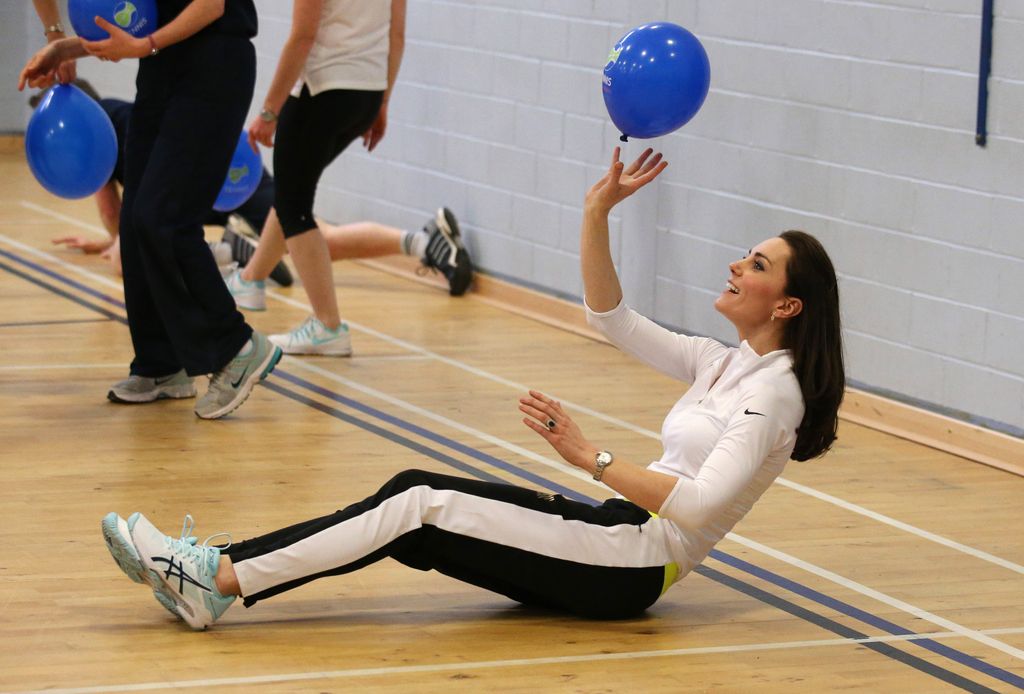 Kate sitting on floor in sports hall hitting balloon