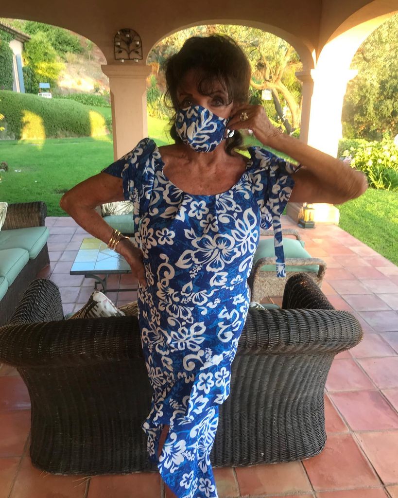 Joan Collins in a blue floral dress and matching face mask