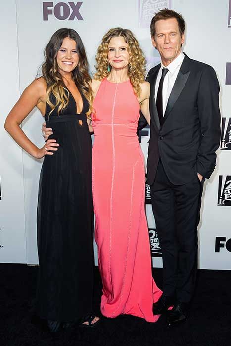 Kyra on a red carpet in a long pink dress with her daughter Sosie on the left and husband Kevin on the right