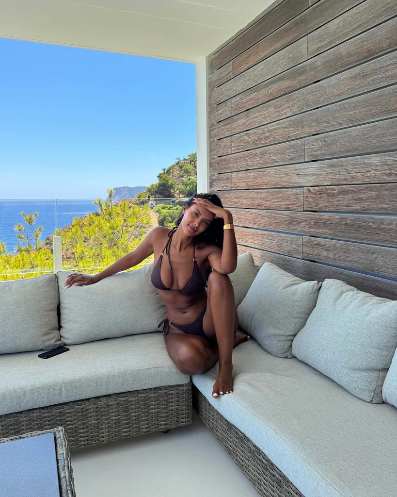 Maya Jama sits on a terrace in a chocolate brown string bikini with gold detailing