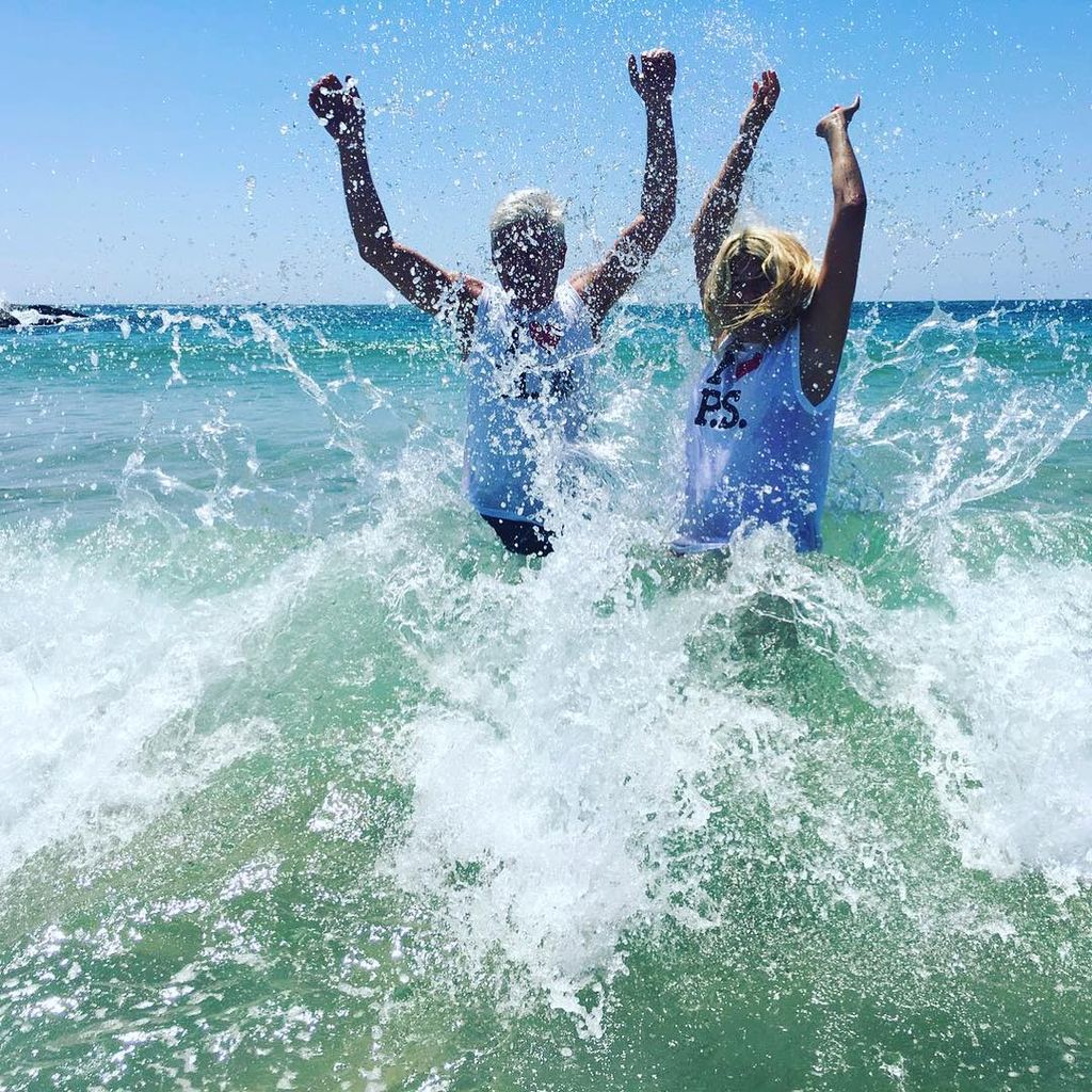 Phillip and Holly throw their arms up in the air while jumping in the sea