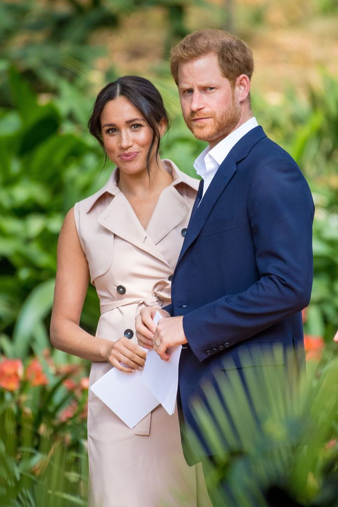 meghan markle in trench dress and prince harry in navy suit in garden