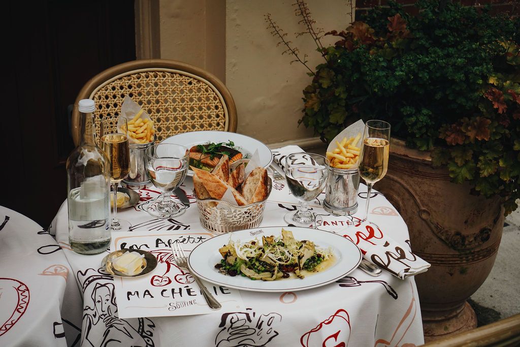 table with printed tablecloth and french food on plates with glasses of wine