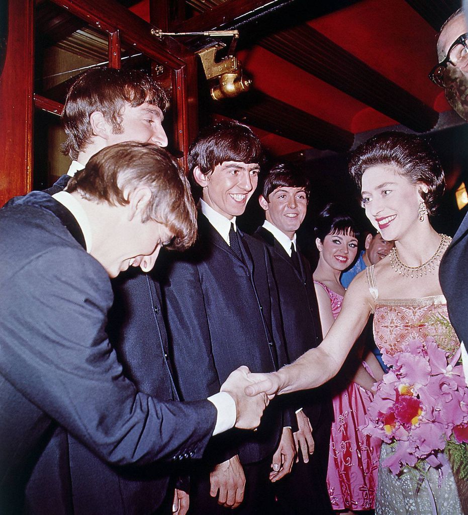 The Beatles, suited in matching dark jackets, meet Princess Margaret. Ringo bows deeply as the others smile beside him. It’s formal meets fangirl in a royal backstage moment.