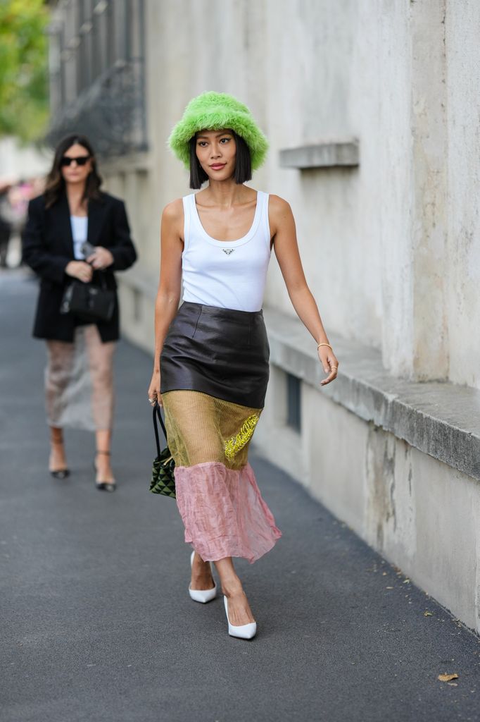 Molly Chiang walks down the street wearing a white tank top, tiered skirt and green fluffy hat