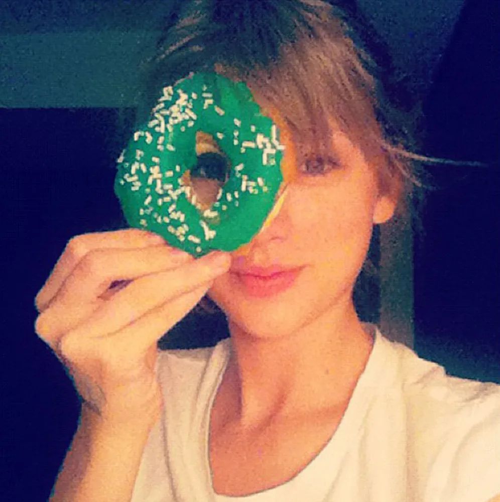 Taylor Swift holds up a green donut to her eye 