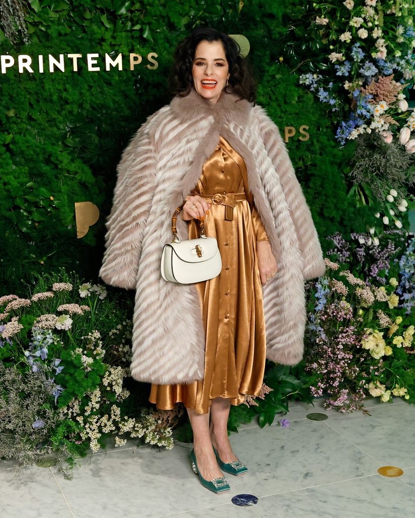 Parker Posey mengenakan gaun emas dan mantel bulu menghadiri pembukaan Printemps New York di One Wall Street pada 20 Maret 2025 di New York City.