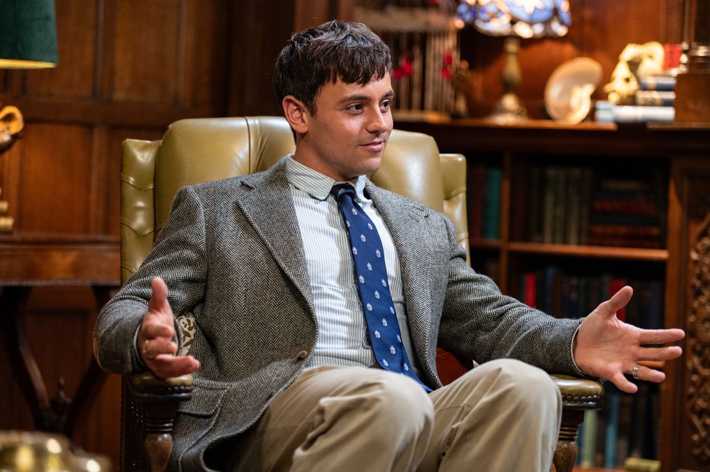 Tom Daley in a suit and tie sitting in an armchair