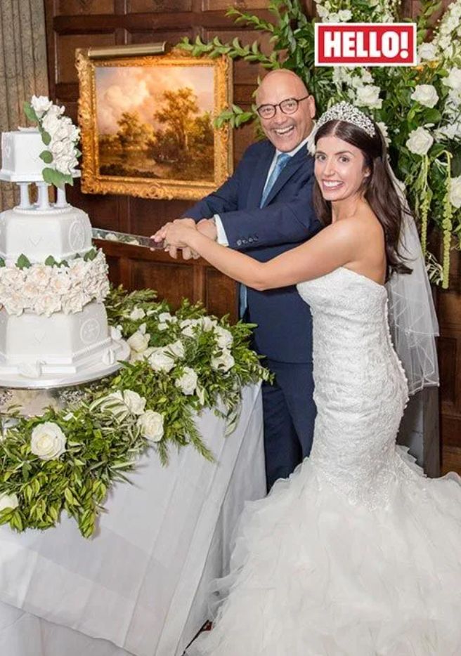 Gregg Wallace in a blue suit and Anne-Marie Sterpini in a bridal gown slicing into a wedding cake