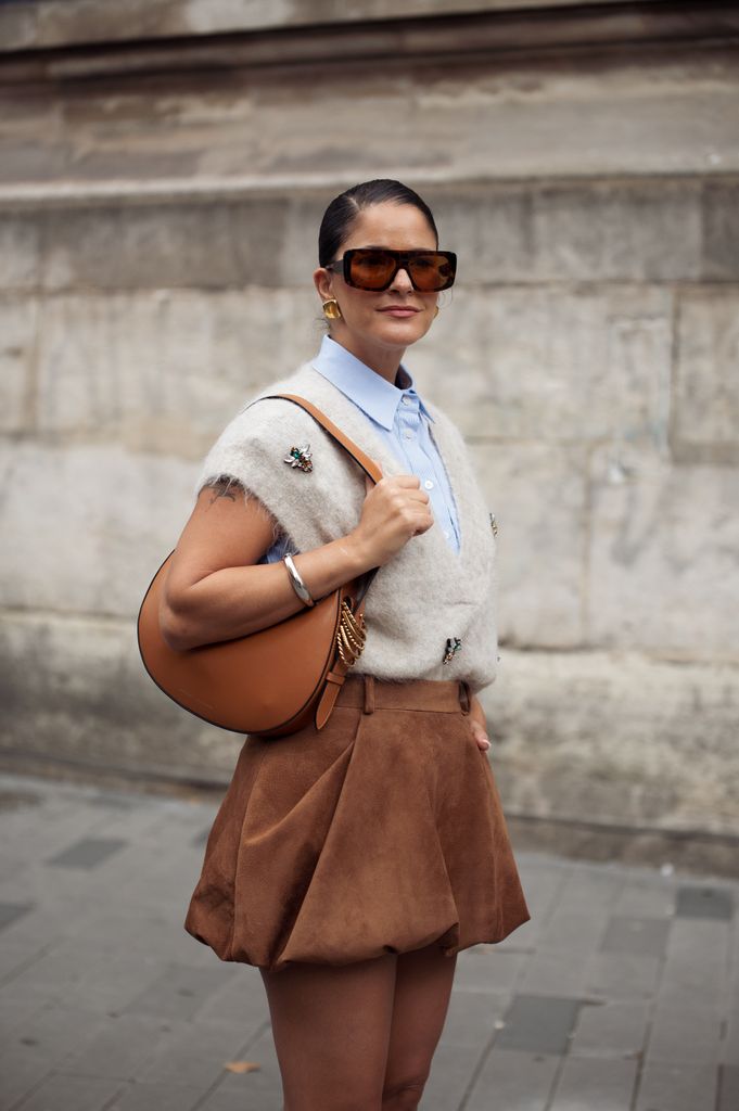 Gili Biegun wears brown balloon skirt, light blue shirt, beige knitted vest with accessories, brown bag and brown sunglasses outside the Vivienne Westwood show during Womenswear Spring/Summer 2025 as part of  Paris Fashion Week on September 28, 2024 in Paris, France.