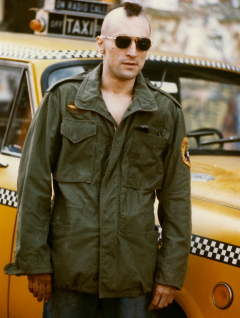Robert De Niro, as Travis Bickle in the 1976 Martin Scorsese film 'Taxi Driver', with his iconic Mohawk haircut standing by a New York Yellow Taxi Cab.