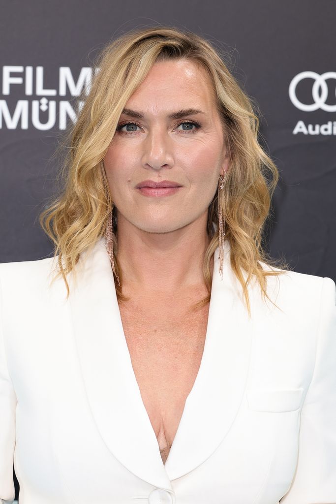 Kate Winslet slightly smiling in a white suit