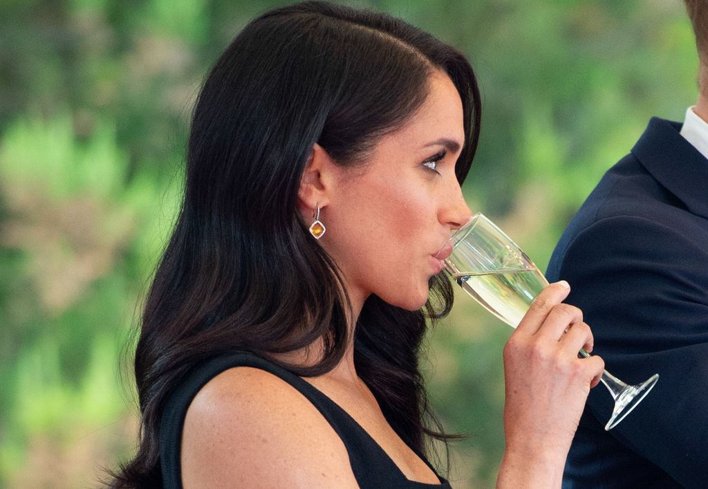 Duchess of Sussex sipping champagne in a black dress