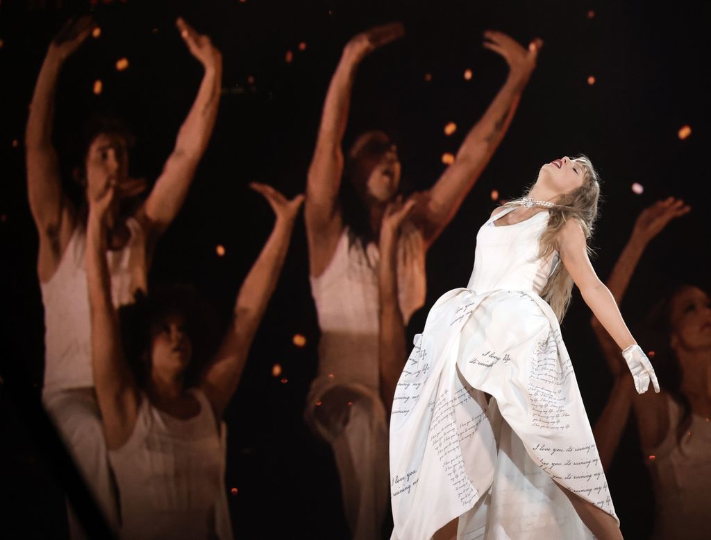 Taylor Swift in a white dress on stage leaning back