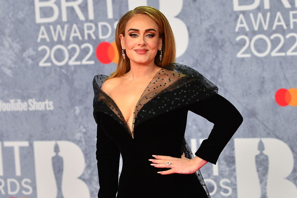 Adele smiling with her hand on her hip, a large ring is on her ring finger
