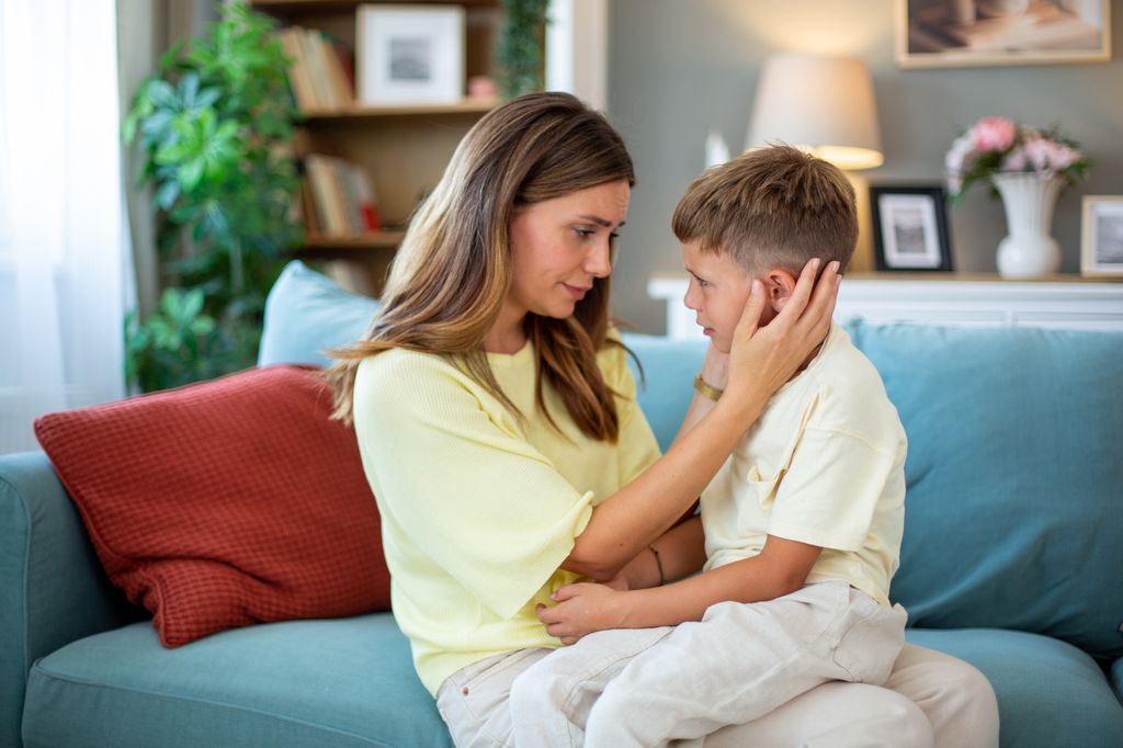 Mother comforting her sad son, holding his face and looking at him with love and compassion
