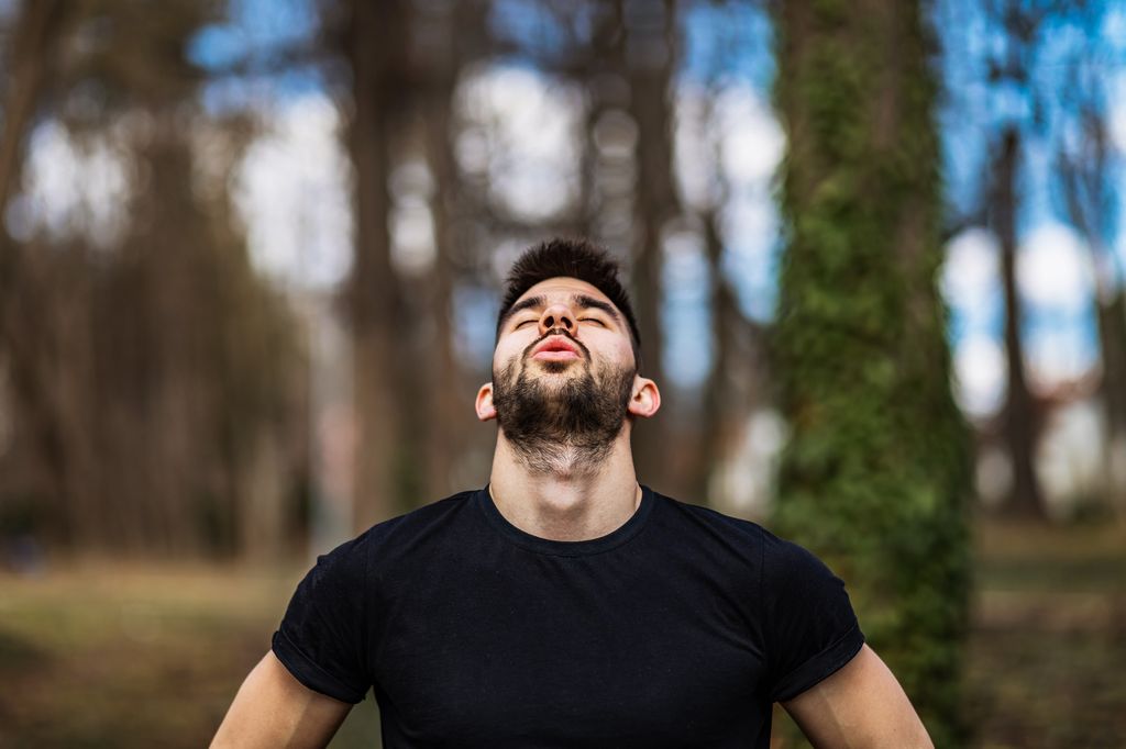 Happy casual man breathing fresh air in a park with trees in the background