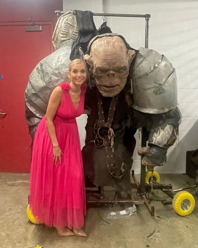 presenter posing with troll while wearing hot pink dress 