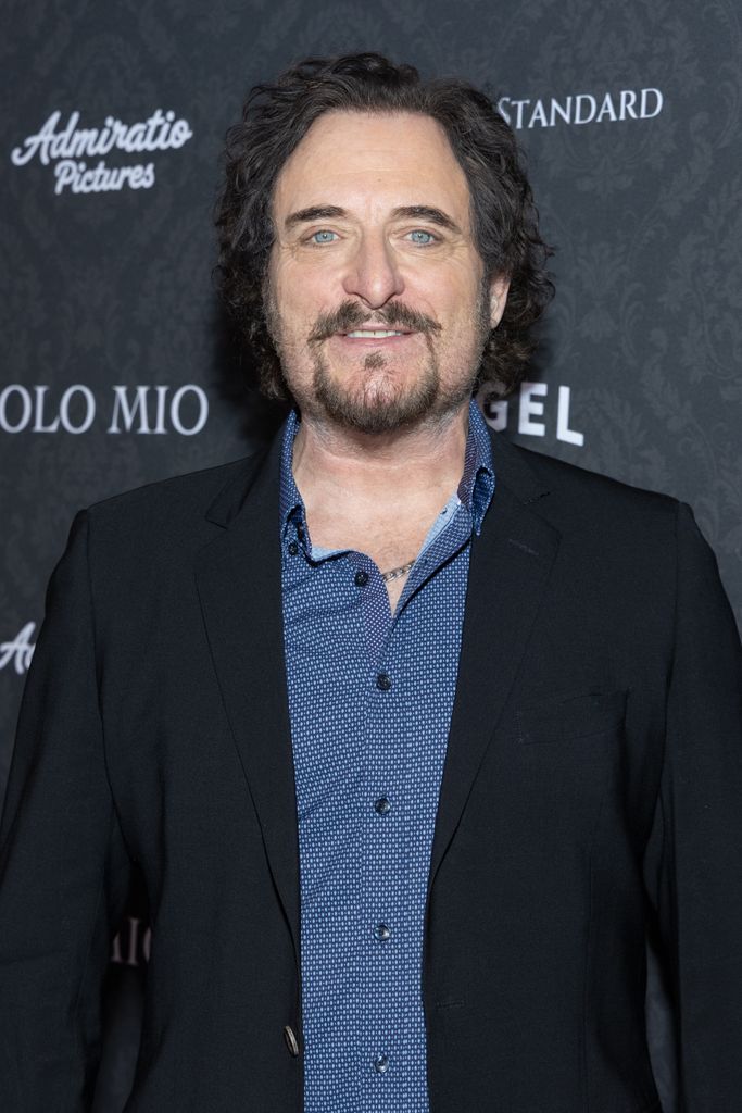 Kim Coates porte une veste noire et une chemise bleue en jean. Il se tient devant une toile de fond avec le logo de son dernier film Solo Mio.