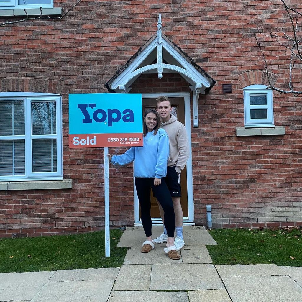 Chloe Hewitt and George Betts holding sold sign outside house