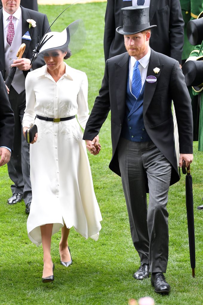 Meghan Markle in a white dress and black belt holding hands with Prince Harry at Royal Ascot 2018