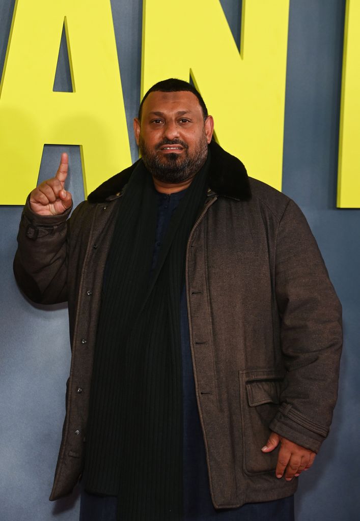 Naseem Hamed in a brown coat pointing at a sign