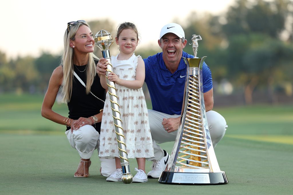 Rory McIIroy smiling on the right, with his arm around his daughter, Poppy and his wife, Erica on the left smiling