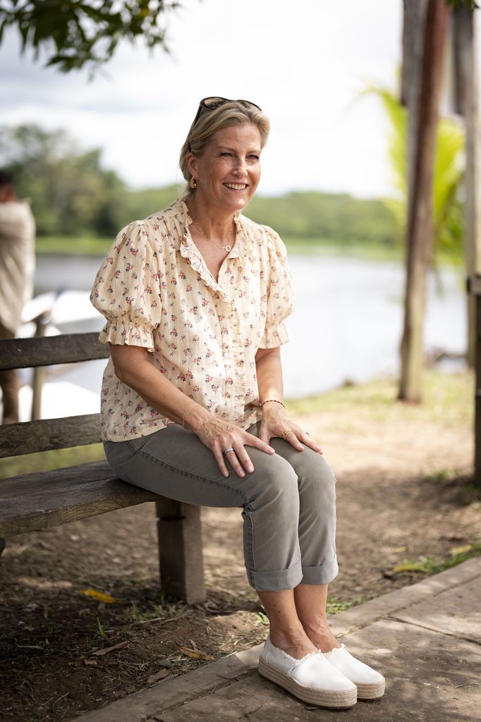 The Duchess of Edinburgh sat outside on bench wearing cargo pants and floral blouse