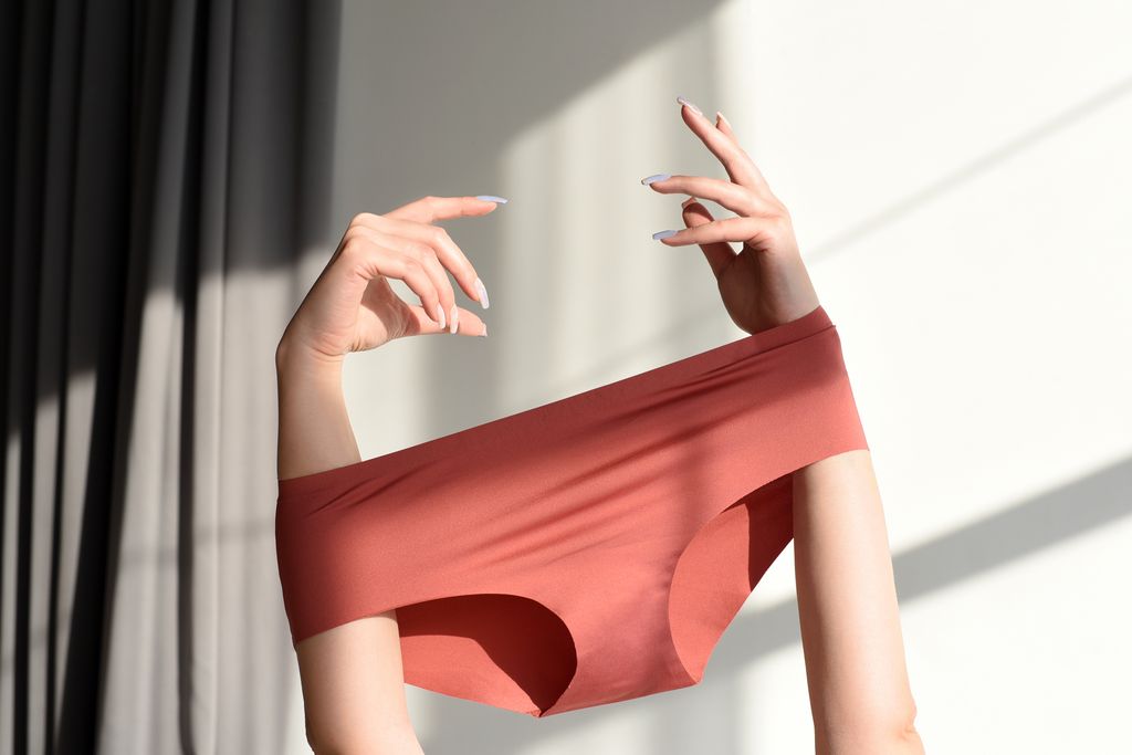 Seamless female panties in the hands of a woman. White background with sun shadow.
