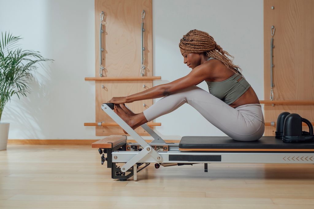  woman touching toes while doing pilates exercise on reformer.
