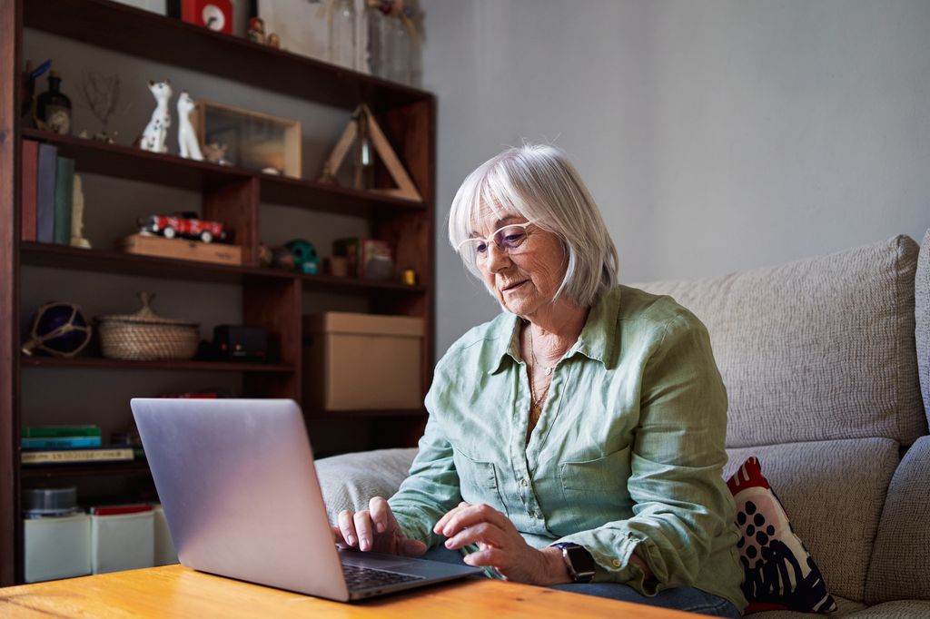 Portrait of a senior woman with grey hair using a laptop sitting on the sofa in a house