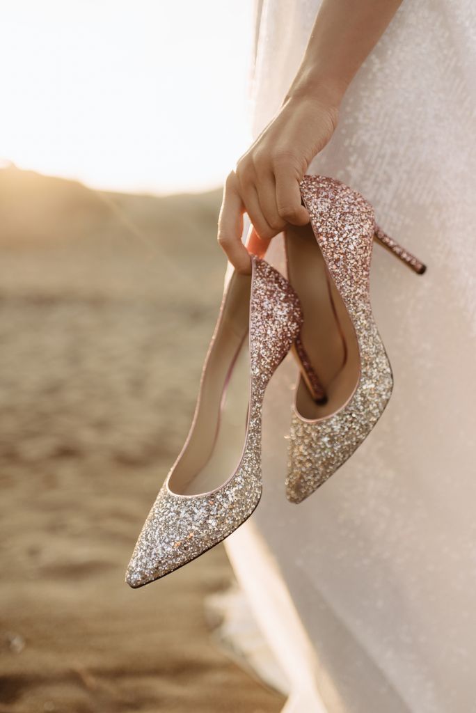 Close up photo of glittery heels in the bride's hands in the sunny day.
