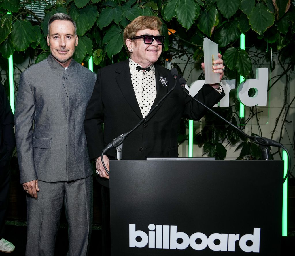 Elton John holding an award with David Furnish behind him