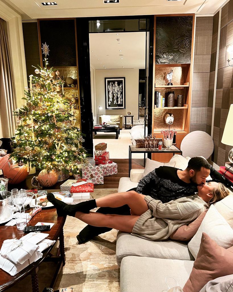 Chrissy and John sharing a kiss in living room with Christmas tree