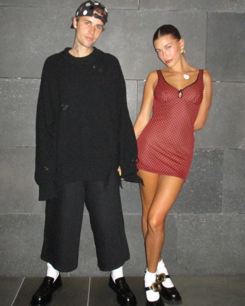 Justin et Hailey Bieber debout devant le mur de briques se tenant la main
