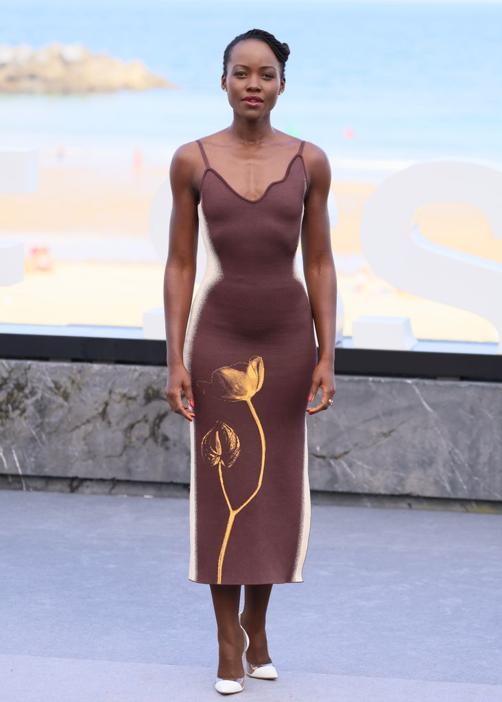 Lupita Nyong'o wears a  fitted brown knit dress with a subtle floral design hugged every curve in the most flattering way. The spaghetti straps and minimalistic design were elevated by a unique, almost abstract floral motif. 