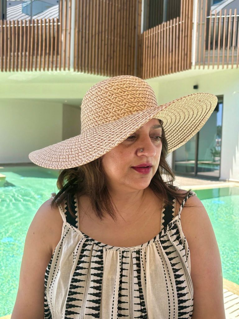 woman in a sun hat and strappy dress in front of a swimming pool