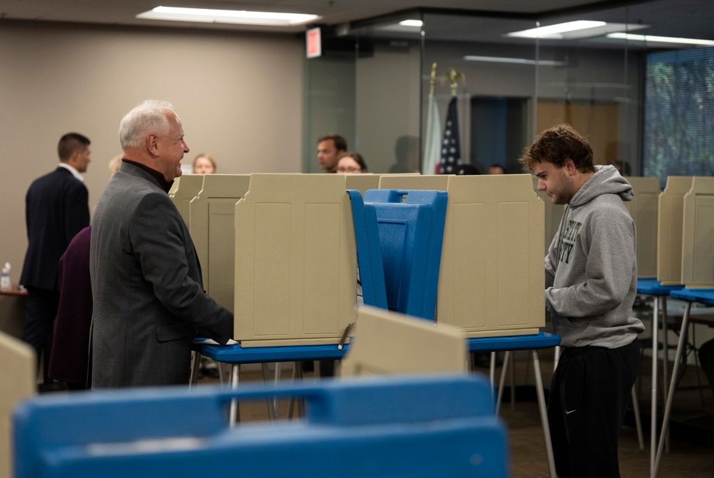 Minnesota Gov.Tim Walz, the Democratic nominee for vice president, left, talks with his son Gus, a first-time voter, as they fill out their ballots at Ramsey County Elections in St. Paul, Minn., on Wednesday, Oct. 23, 2024