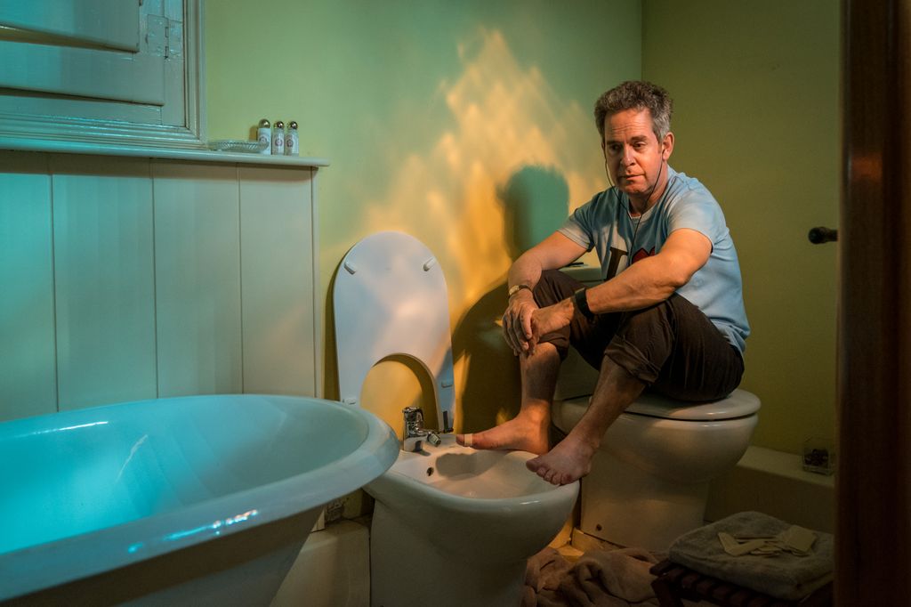 man sitting on toilet seat in bathroom