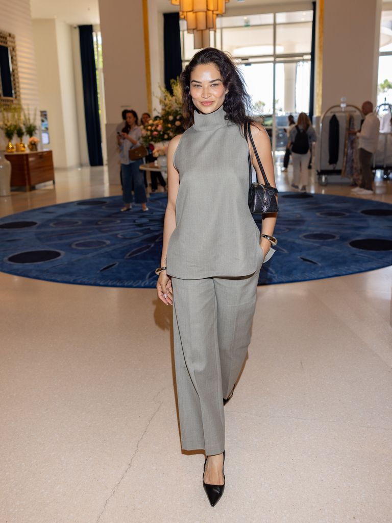Shanina Shaik wears a high neck top and matching grey trousers with pointed black heels.