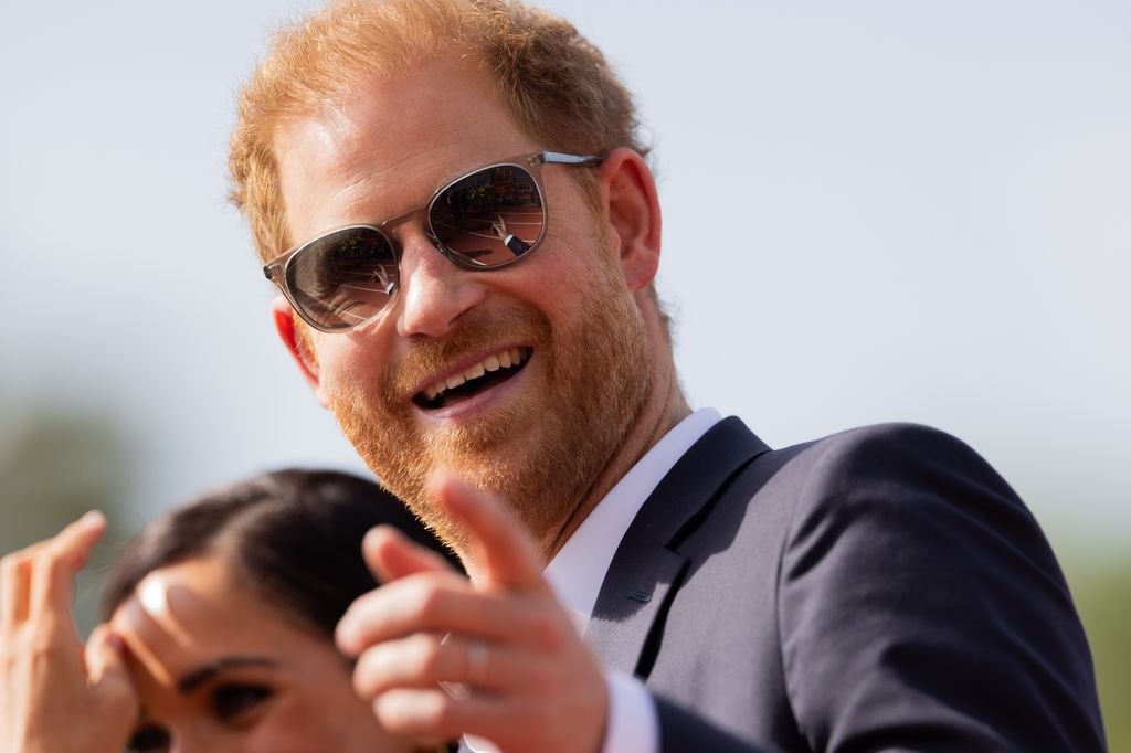 Prince Harry wearing sunglasses as he points to the camera
