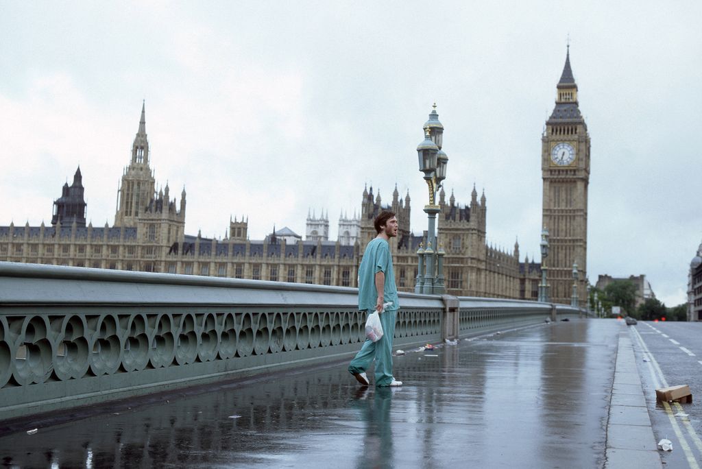 Cillian Murph wearing turquoise medical scrubs walking along waterloo bridge with Big Ben in the background
