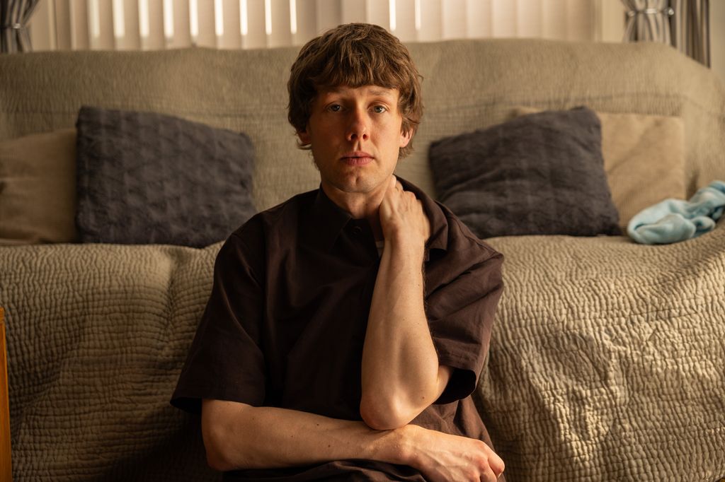 Josh Finan sitting by a sofa in a scene from Waiting for the Out