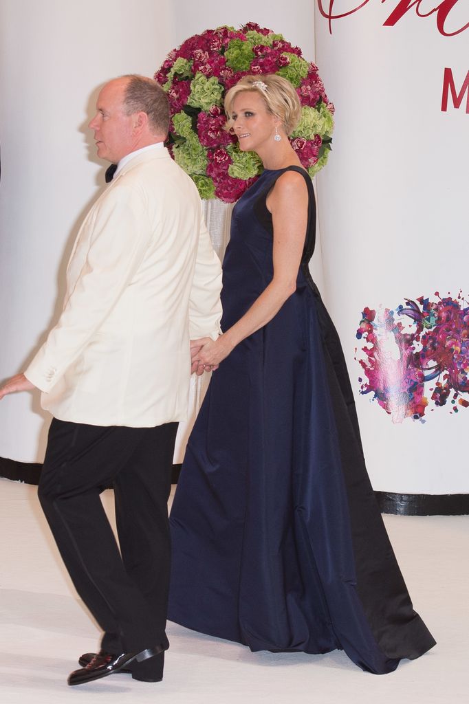 Princess Charlene in a blue gown holding hands with her husband