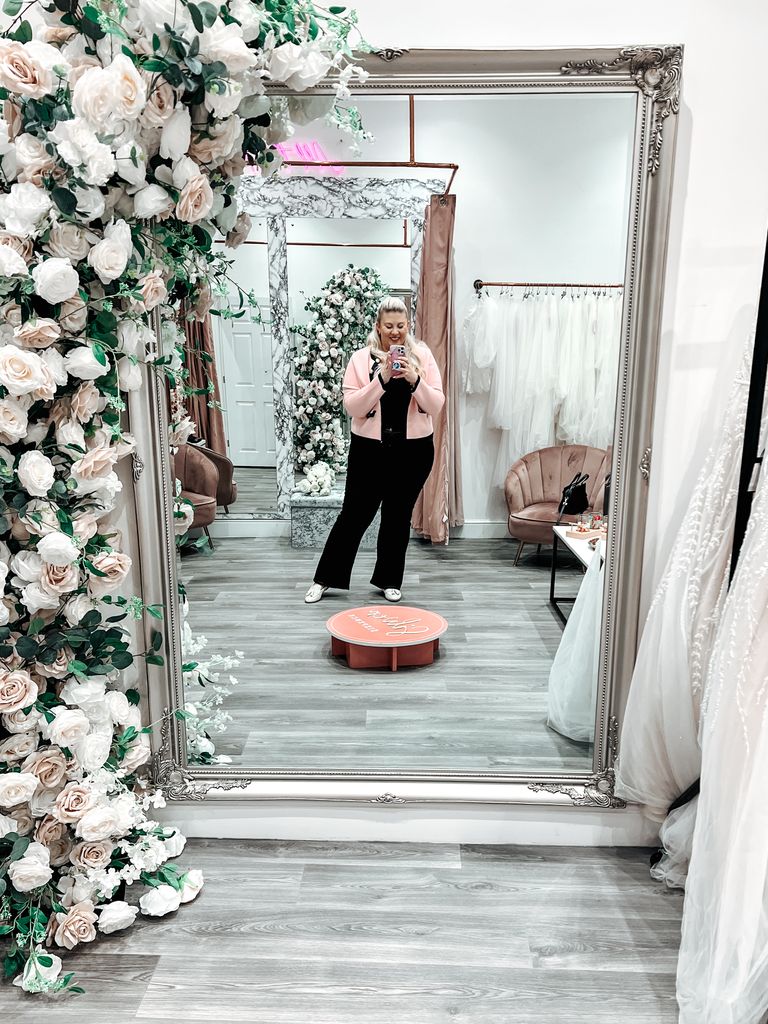 Woman taking mirror selfie in wedding dress shop